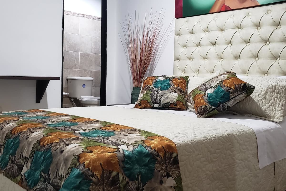 A neatly made bed with a floral bedspread, a tufted headboard, and a bedside table with a drawer.