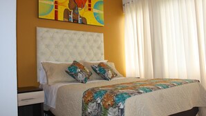 A bedroom with a tufted headboard, a bed with a floral-patterned bedspread, and a painting above the bed. - Hotel San Blass (La Unión)