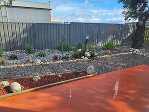 A landscaped garden with a variety of plants and rocks, a wooden fence, and a red paved area.