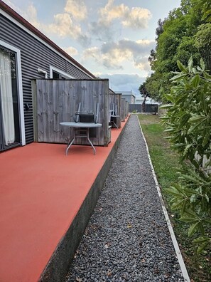 A row of outdoor seating areas with tables and chairs, separated by wooden partitions, along a gravel path with a red surface.