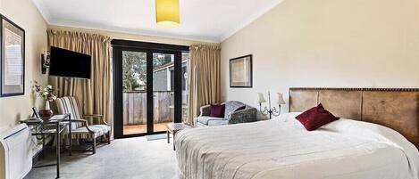 Habitación de hotel con una cama grande, un escritorio con una silla, televisión y una puerta corrediza de vidrio al exterior.
