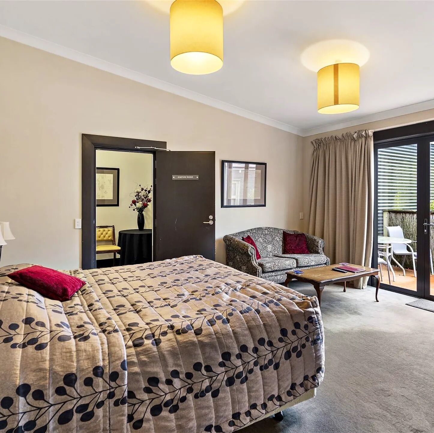 A hotel room with a bed, a sofa, a small table, and a door leading to a balcony.