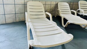 A row of white plastic lounge chairs with a tiled floor and a window in the background.