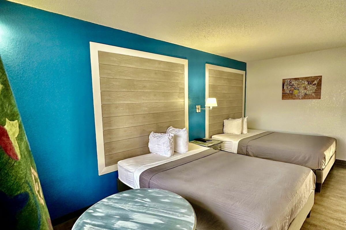 A hotel room with two beds, a small round table, and a wall-mounted mirror.