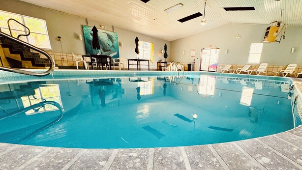 An indoor swimming pool with a wooden deck, lounge chairs, and a ceiling fan.