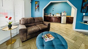 A living room with a brown leather sofa, a blue ottoman, and a small round table with a potted plant.