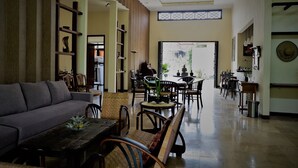 A spacious living area with a sofa, dining table, and chairs. There is a bookshelf and a view of the outside through a large door. - Villa Kendi (Glenmore)