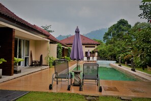Poolbereich mit zwei Stühlen und einem Tisch, umgeben von üppiger Bepflanzung und Bergblick.