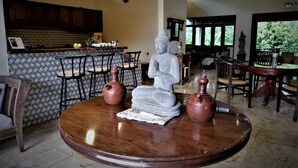 A room with a round wooden table, a Buddha statue, and two pottery pieces. There are chairs around the table, and a kitchen area with a patterned backsplash and wooden cabinets. - Villa Kendi (Glenmore)