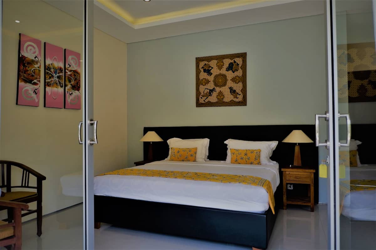 Quarto moderno com uma cama grande, uma cadeira de madeira e uma mesa de cabeceira com luminária.