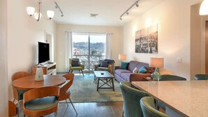 Una sala de estar moderna con comedor, un juego de sofá, televisor y un amplio ventanal con vista a la ciudad.