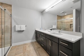 Een moderne badkamer met een douchecabine van glas, een grote spiegel en een wastafelmeubel met dubbele wastafel.