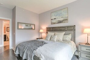 Een slaapkamer met een bed, nachtkastjes, een schilderij en een spiegel.