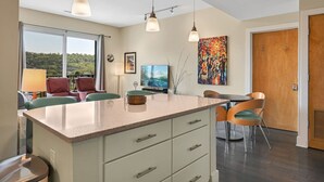 A modern kitchen with a central island, pendant lighting, and a dining area with chairs. - Balcony Condo in Downtown Asheville (Asheville)