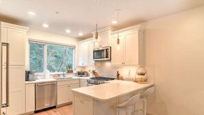 A modern kitchen with white cabinetry, stainless steel appliances, and a large island with bar stools. - 243 Short Coxe Ave Townhome (Asheville)