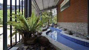 A swimming pool with a tiled edge, surrounded by rocks and plants, and a wooden wall in the background. - A-SAN Hot Spring Hotel (Jiaoxi)