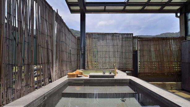 A spa area with a hot tub, bamboo walls, and a view of the mountains. - A-SAN Hot Spring Hotel (Jiaoxi)