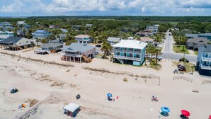 Vista aérea de uma cidade costeira com propriedades à beira-mar, uma praia de areia e céu claro.