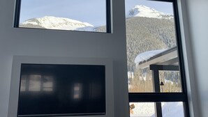 A room with a large window overlooking a snowy mountain and forest.