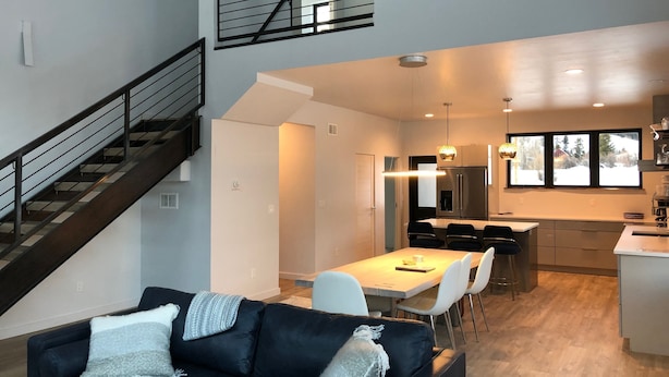 A modern kitchen with a dining area, a staircase, and a living room with a sofa.