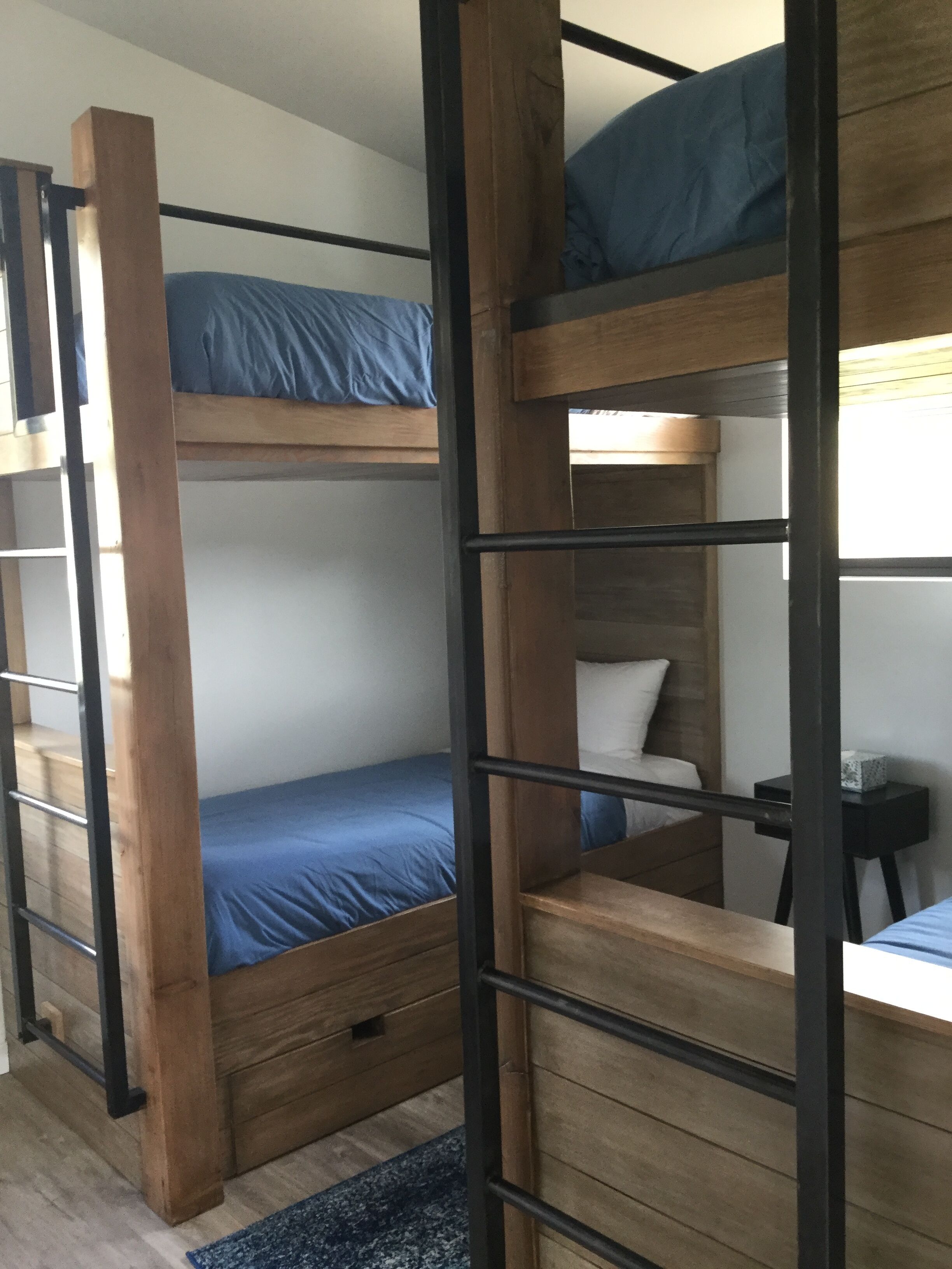 A bunk bed with a wooden frame, a single bed below, and a small table with a lamp.