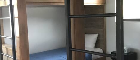 A bunk bed with a wooden frame, a single bed below, and a small table with a lamp.