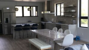 A modern kitchen with a dining area, featuring a large island, bar stools, and a bench.