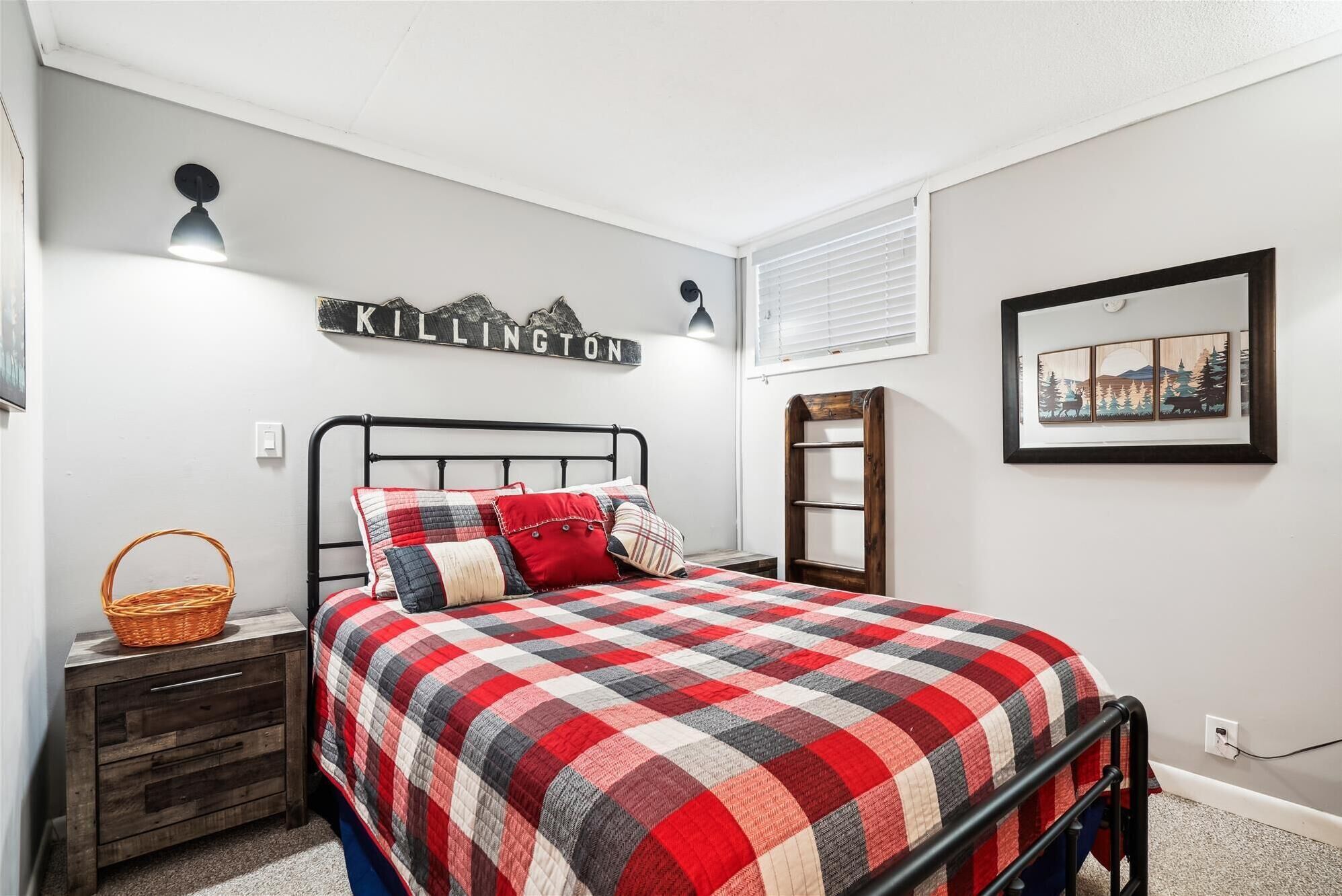 A bedroom with a bed, a nightstand, a wall-mounted shelf, a framed picture, and a wall sign.