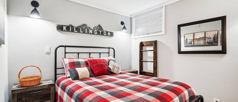 A bedroom with a bed, a nightstand, a wall-mounted shelf, a framed picture, and a wall sign.