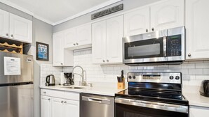 Una cocina moderna con muebles blancos, electrodomésticos de acero inoxidable, microondas integrado, lavavajillas y estufa.