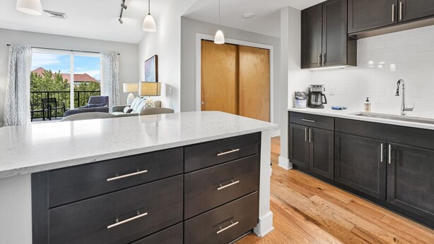 A modern kitchen with dark cabinets, a large island, and a view to a balcony. - Roomy and Accessible Downtown Balcony Condo (Asheville)