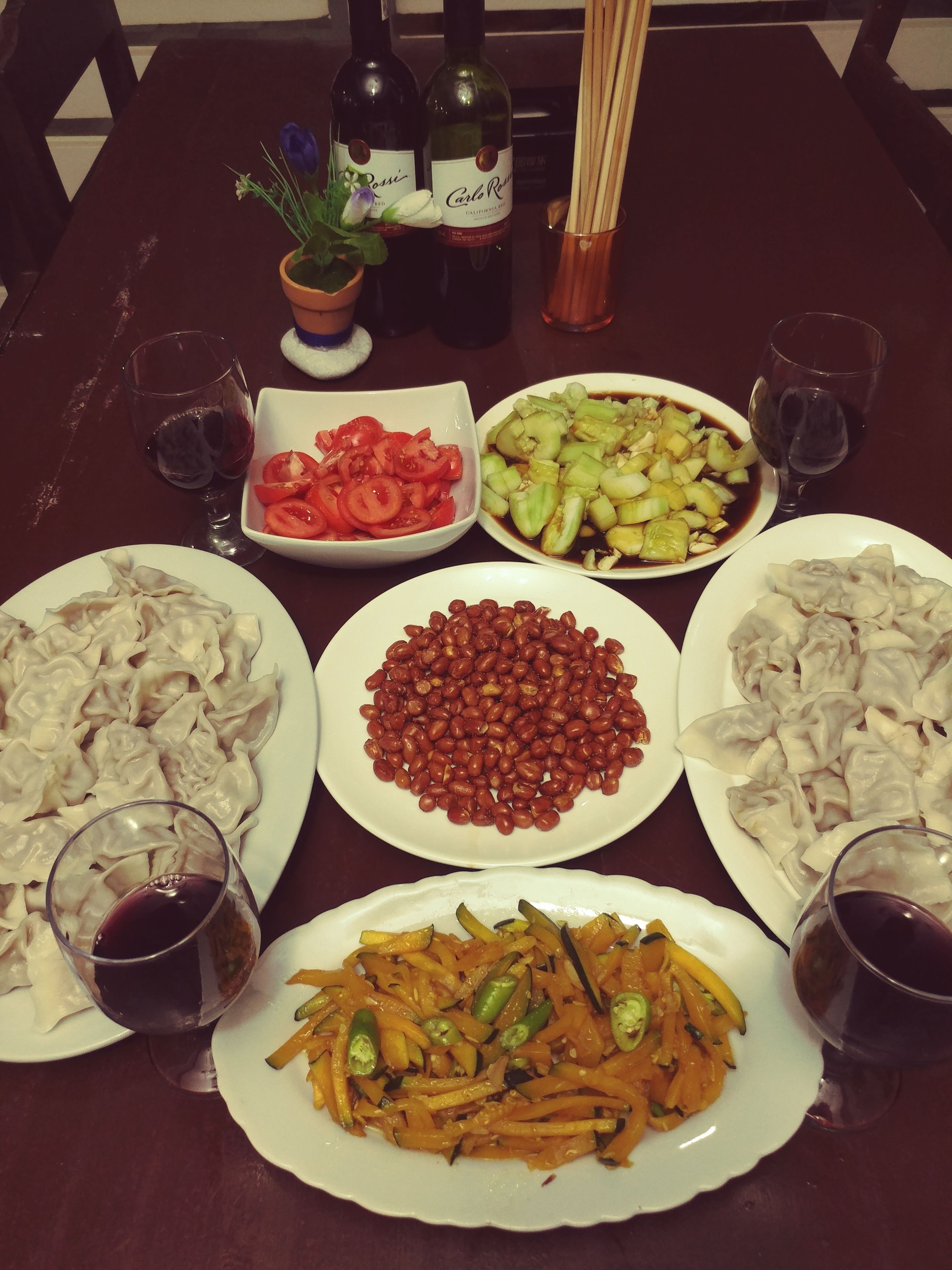Une table à manger avec divers plats, notamment des raviolis, des haricots et des légumes, ainsi que deux bouteilles de vin.