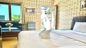 A hotel room with a bed, a desk with a vase of flowers, a refrigerator, and patterned wallpaper. - Dolphin Bay Resort Puerto Galera (Puerto Galera)