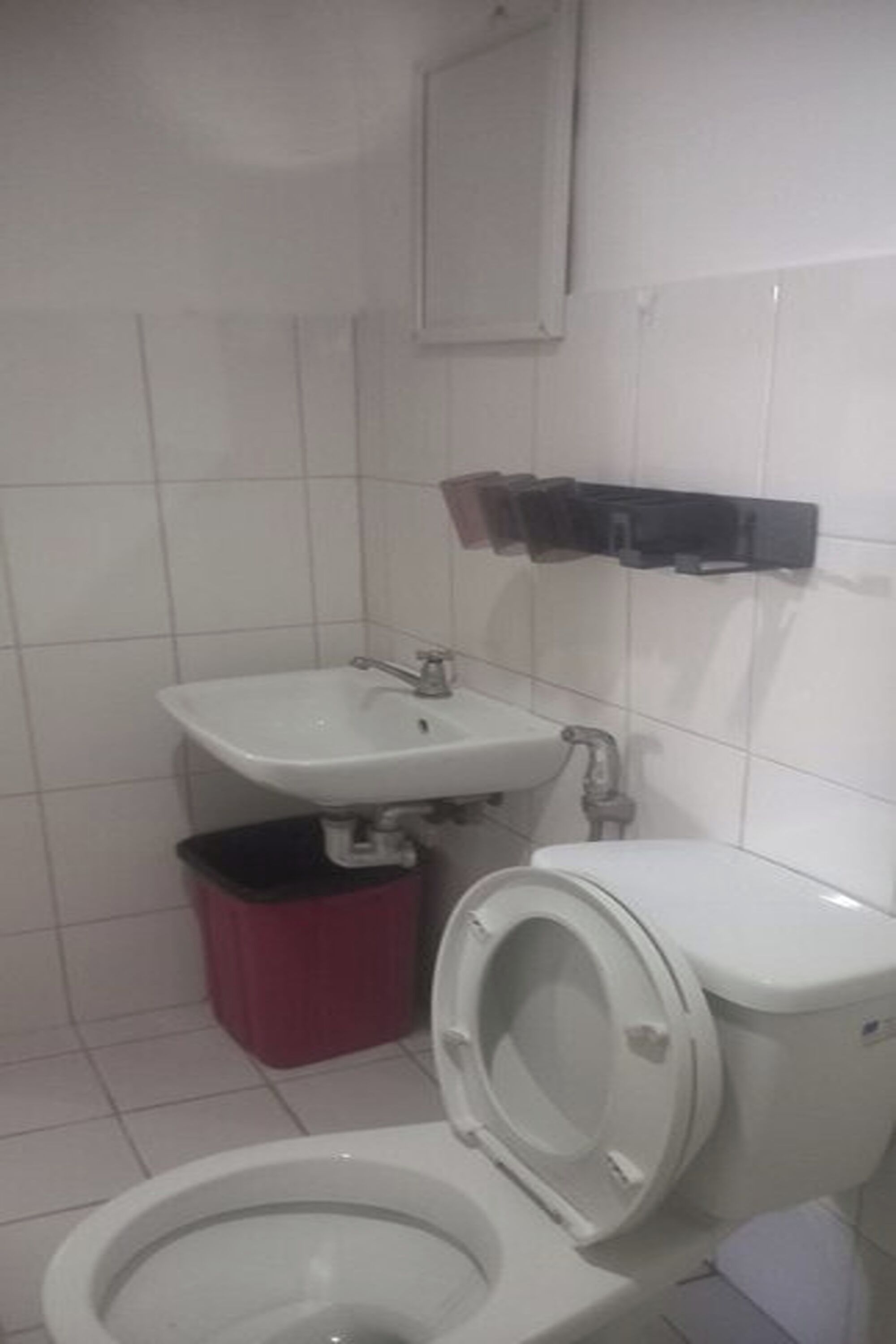 A small bathroom with a toilet, sink, and trash bin.