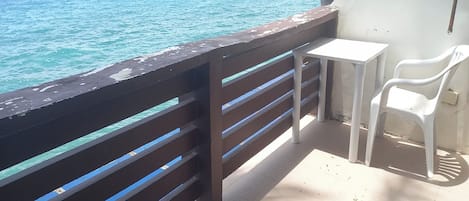 A balcony with a view of the sea, a small table, and two white chairs.