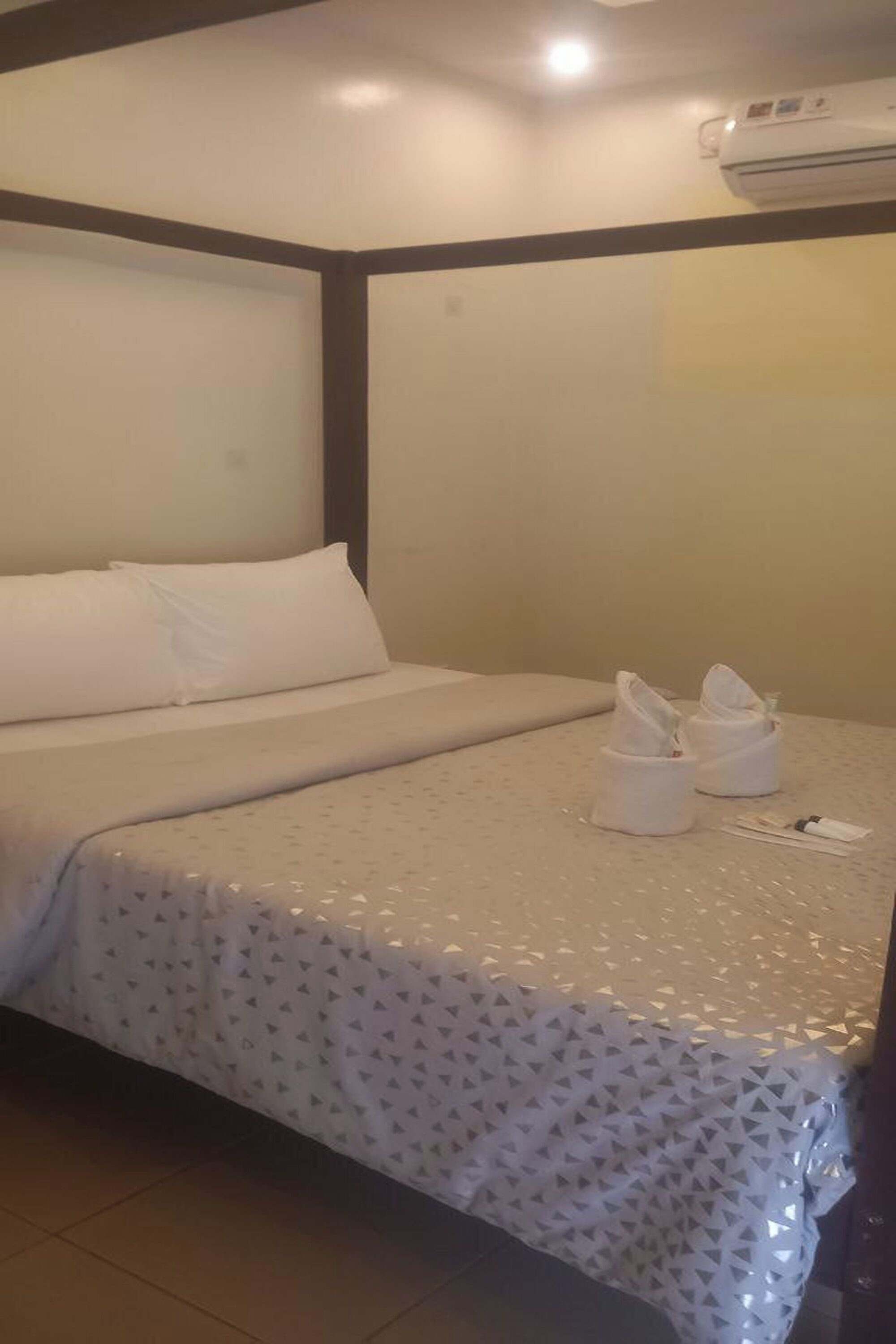 A hotel room with a bed, a wall-mounted air conditioner, and a pair of towels on the bed.