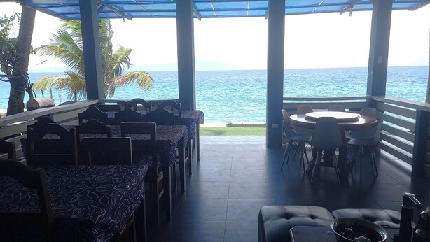 A covered outdoor seating area with tables and chairs, overlooking the ocean. - Dolphin Bay Resort Puerto Galera (Puerto Galera)