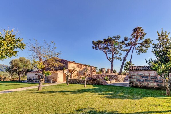 A traditional stone building with a tiled roof, surrounded by a well-maintained lawn and trees.