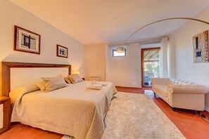 A bedroom with a large bed, a chair, a small table, and a window.