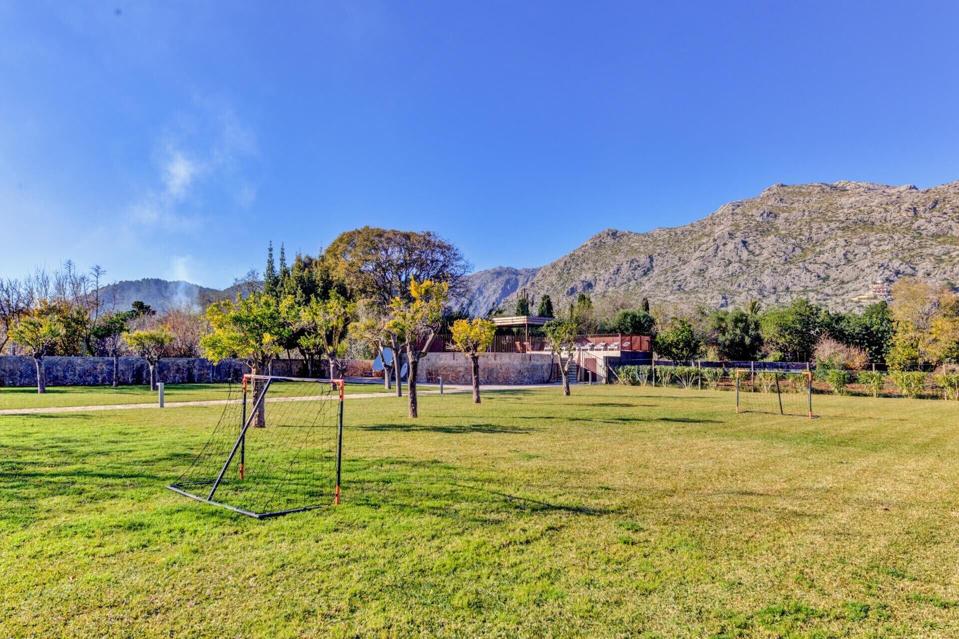 Un champ herbeux avec un but de football, des arbres et une montagne en arrière-plan.