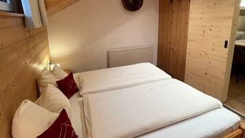 Ein Schlafzimmer mit Holzboden, einem weißen Bett mit roten Kissen, einem weißen Heizkörper und einer Holzwand.