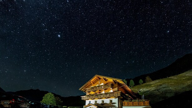 Un edificio de dos pisos con balcones, un estacionamiento y un cielo nocturno estrellado.