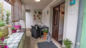 A narrow outdoor corridor with a checkered bench, wicker furniture, potted plants, and a lantern.