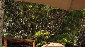 Un área junto a la piscina con tumbonas de madera, una piscina y abundante vegetación.