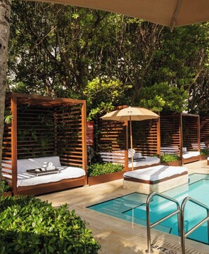Un área junto a la piscina con tumbonas de madera, una piscina y abundante vegetación.