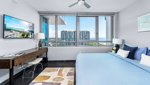 Un hotel moderno con una cama grande, un escritorio, un televisor y vistas de la ciudad a través de amplias ventanas.
