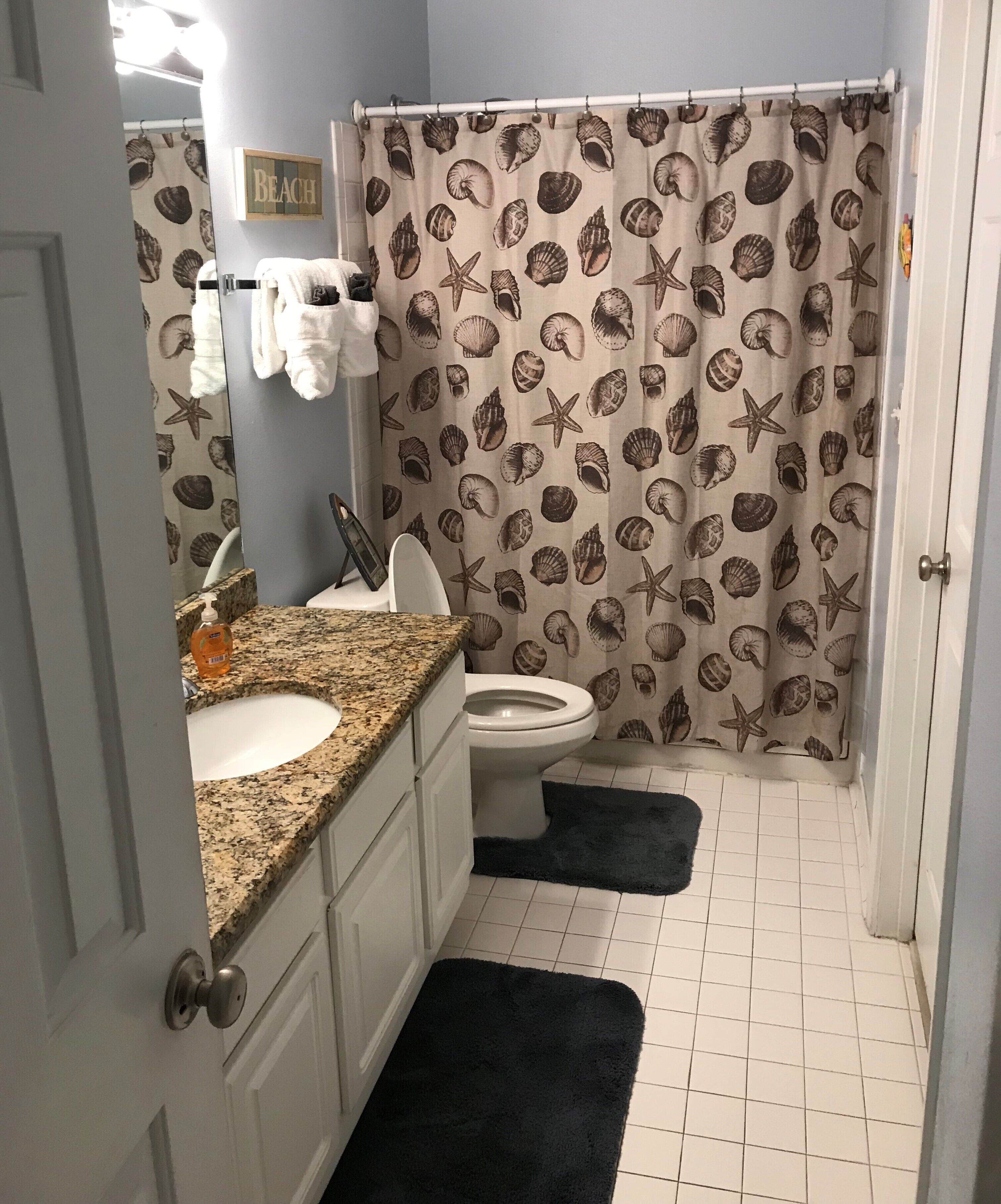 A bathroom with a sink, toilet, and shower curtain with a seashell pattern.