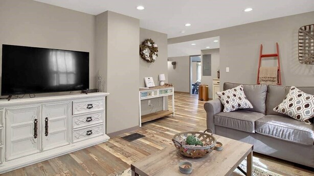A living room with a flat-screen TV, a white cabinet with drawers, a grey sofa with patterned cushions, and a wooden coffee table with a decorative bowl. - The Farmhouse Inn: 3 bed, 3.5 whole house rental (Hermann)