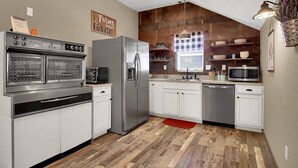 A modern kitchen with stainless steel appliances, white cabinetry, and a wooden floor. - The Farmhouse Inn: 3 bed, 3.5 whole house rental (Hermann)