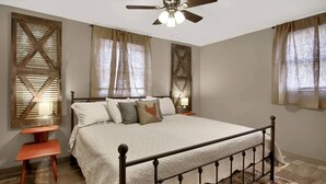 A bedroom with a bed, a nightstand, a chair, a ceiling fan, and windows with curtains. - The Farmhouse Inn: 3 bed, 3.5 whole house rental (Hermann)